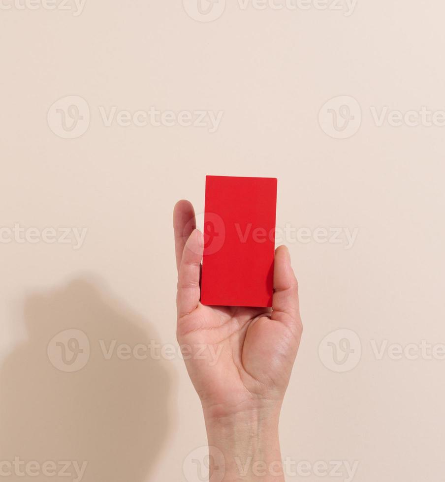 Female hand holding empty red paper on a beige background. Copy paste image or text, close up photo