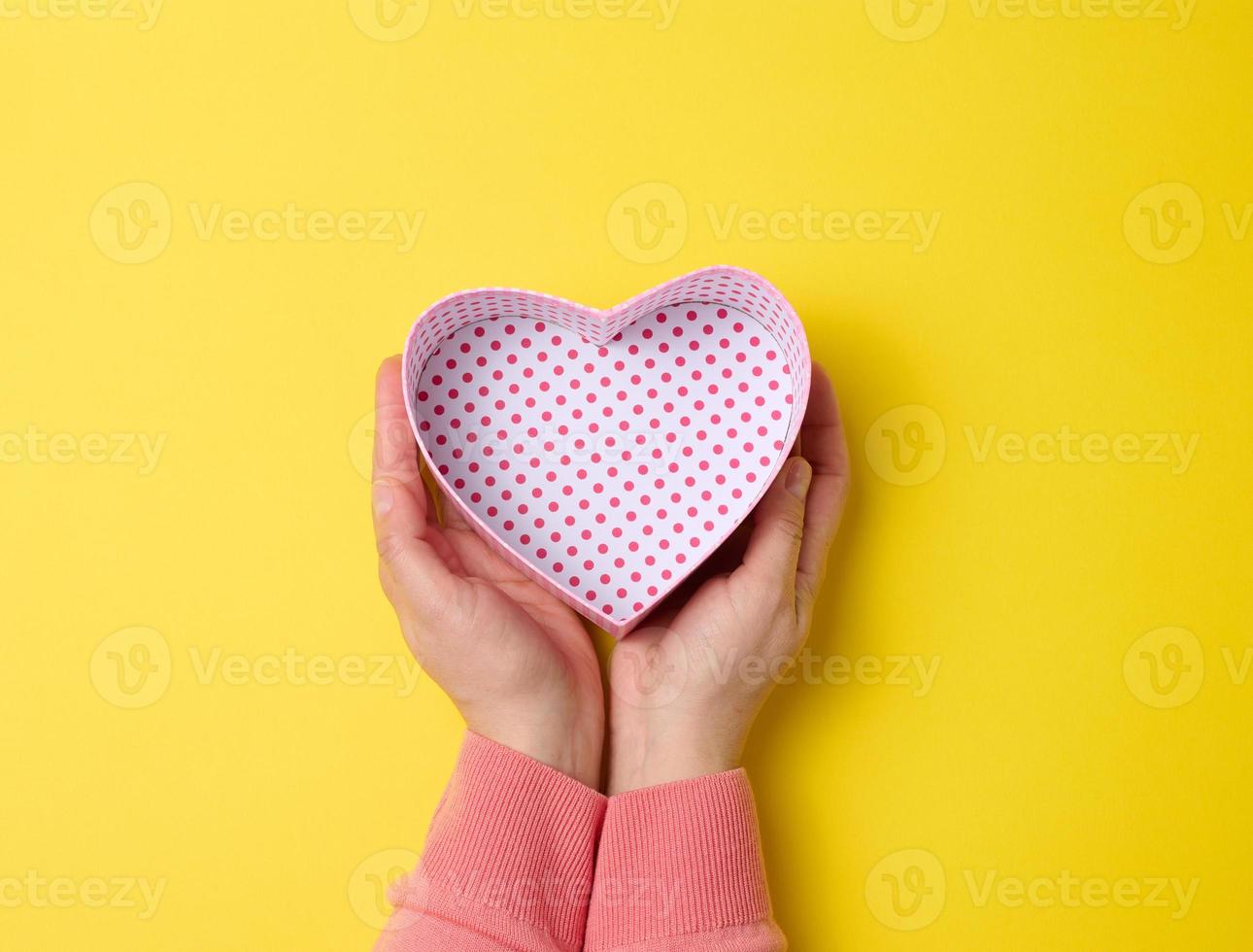 female hands holding open square cardboard gift box on a yellow background, top view photo