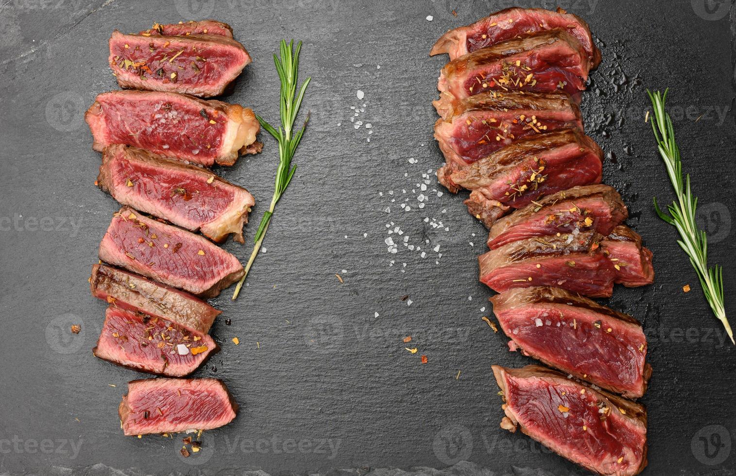 two fried beef steaks cut into pieces on a black board, the degree of doneness rare with blood photo