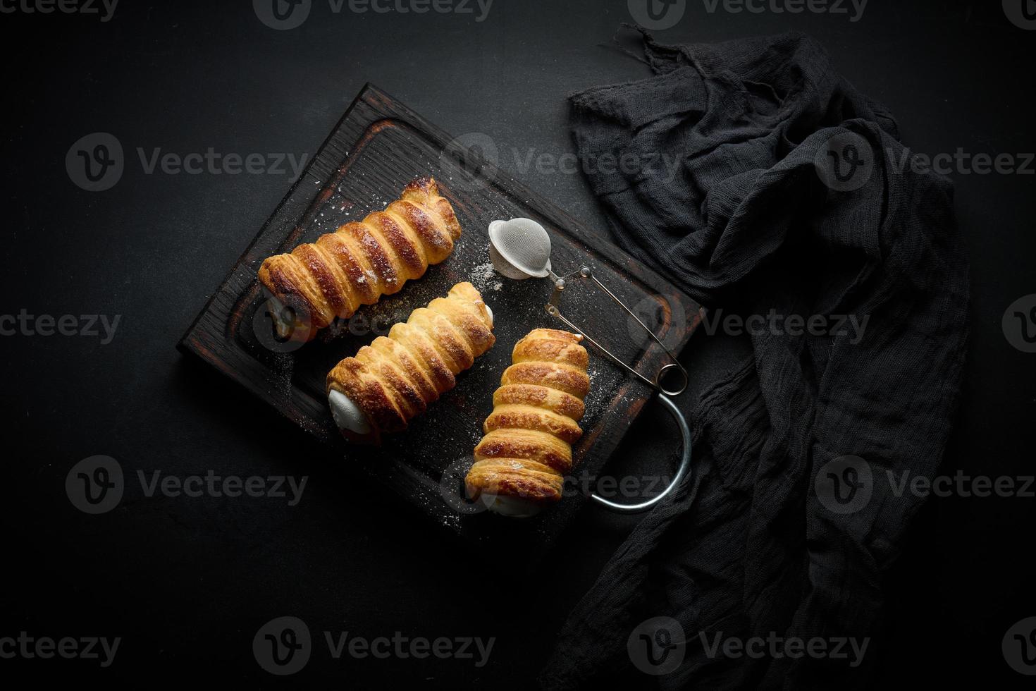 túbulos horneados llenos de crema de clara de huevo batida en una tabla de cocina de madera negra, vista superior foto