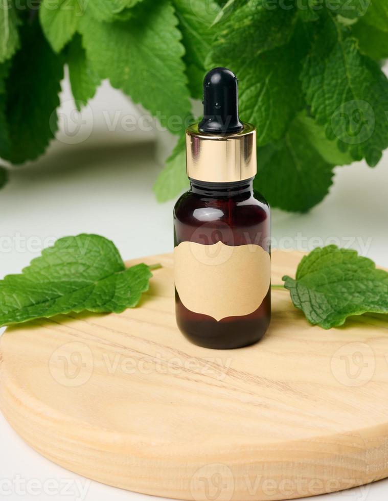Brown glass bottle with paper label and pipette on a white table, green mint leaves photo