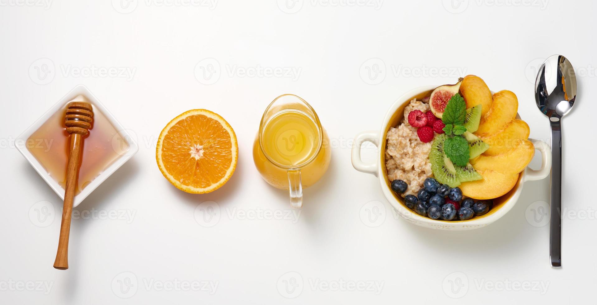 plate with oatmeal and fruit, half a ripe orange and freshly squeezed juice in a transparent glass decanter, honey in a bowl on a white table photo