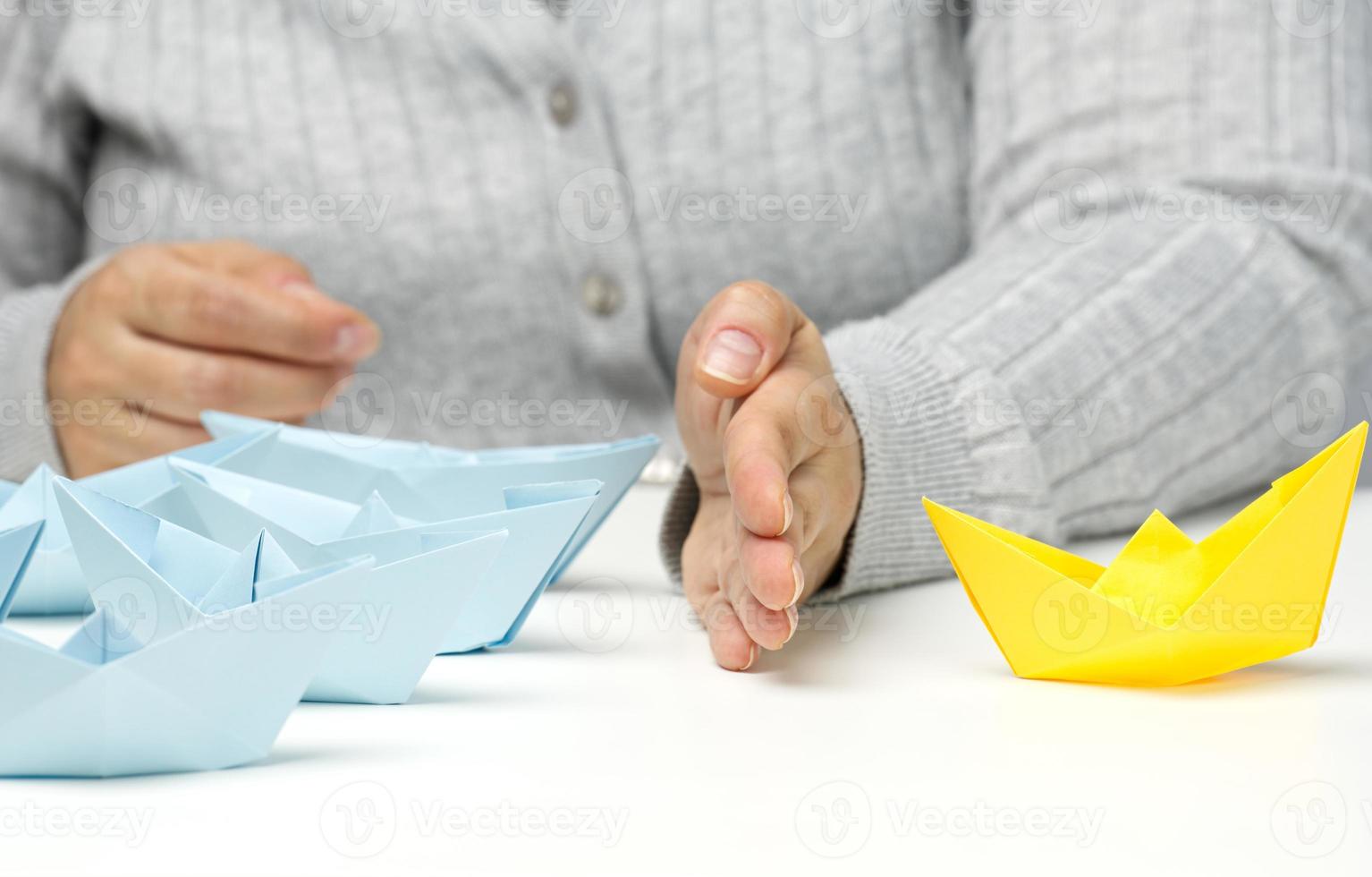 paper boats between a female hand on a white table. Conflict solution concept, negotiator between groups. Searching of decisions photo