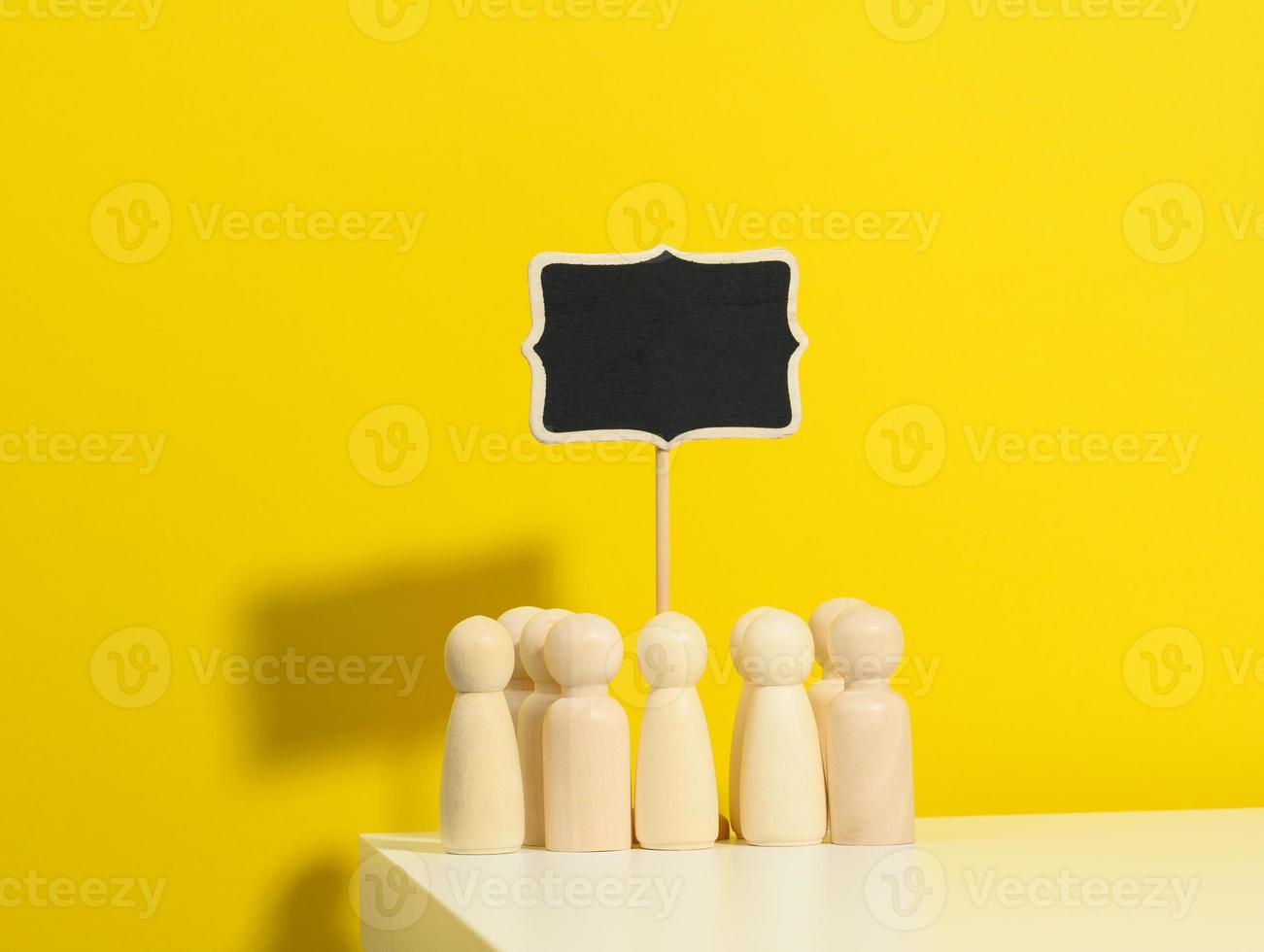 group of wooden figurines and a blank signpost on a yellow background. The concept of gathering people to express their will, demonstration photo