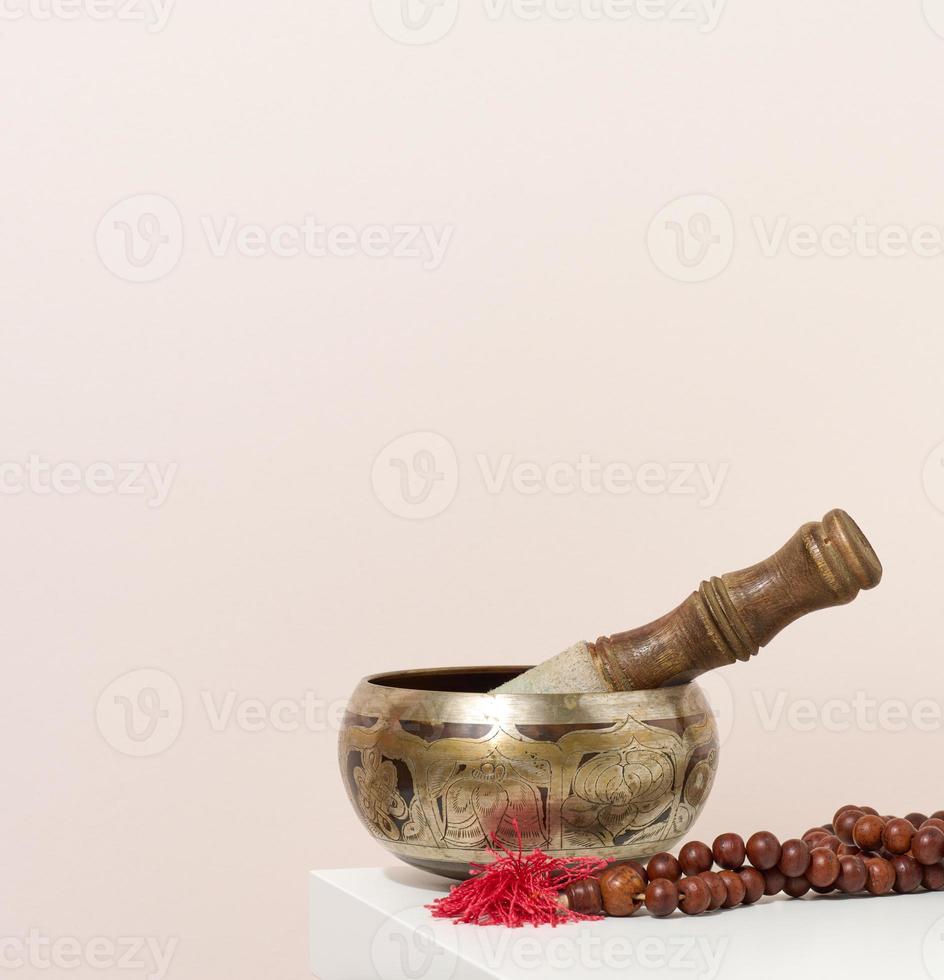 cuenco de cobre y badajo de madera sobre una mesa blanca. instrumento musical para meditación, relajación, diversas prácticas médicas relacionadas con los biorritmos, normalización de la salud mental foto