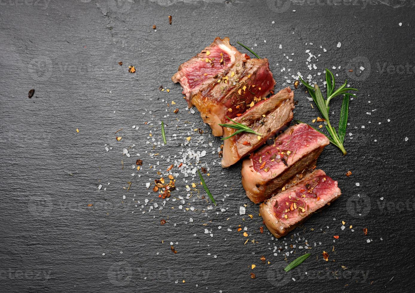 sliced fried beef steak New York  striploin on a black background with spices, degree of doneness rare photo