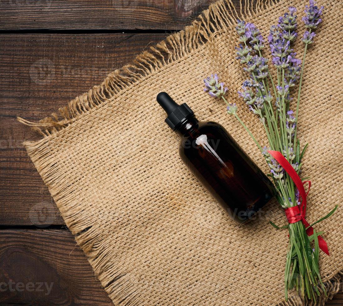 A glass brown bottle with a pipette and a bouquet of lavender on a brown wooden table. photo