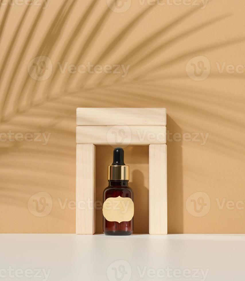 botella de vidrio marrón con pipeta y etiqueta en blanco de papel sobre fondo marrón claro. maqueta de producto cosmético para el cuidado de la piel foto