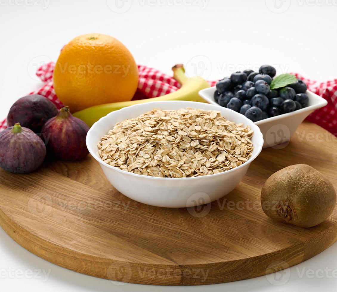 Raw oatmeal in white ceramic plate and fruits on white table, breakfast photo