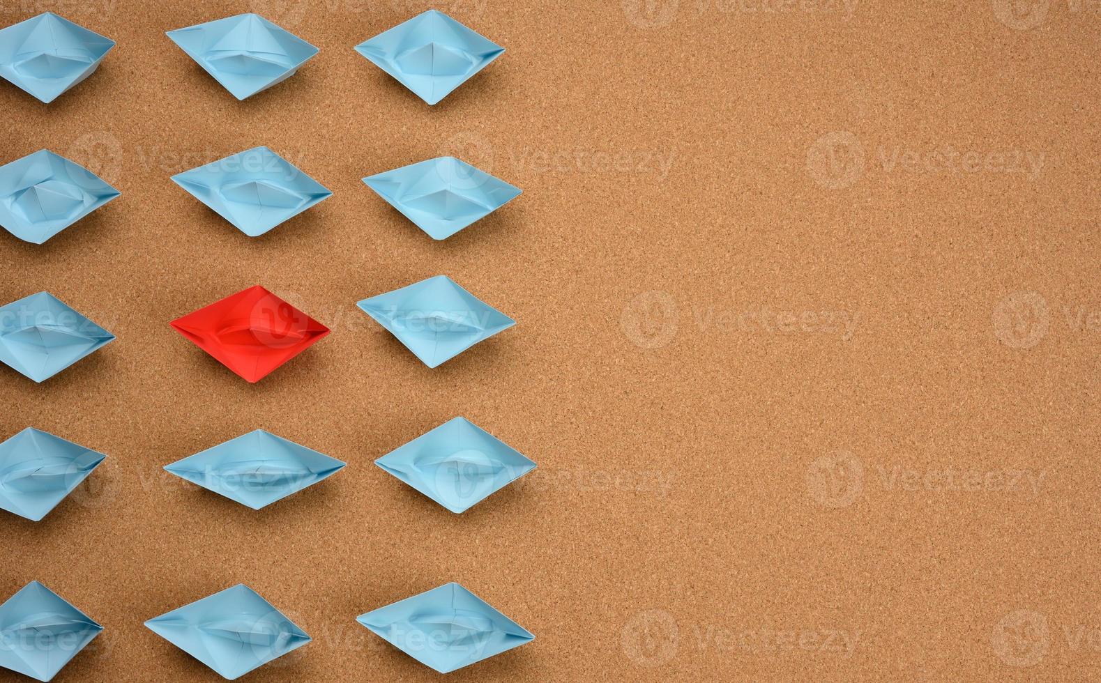 group of blue paper boats and one red in the middle on a brown background photo