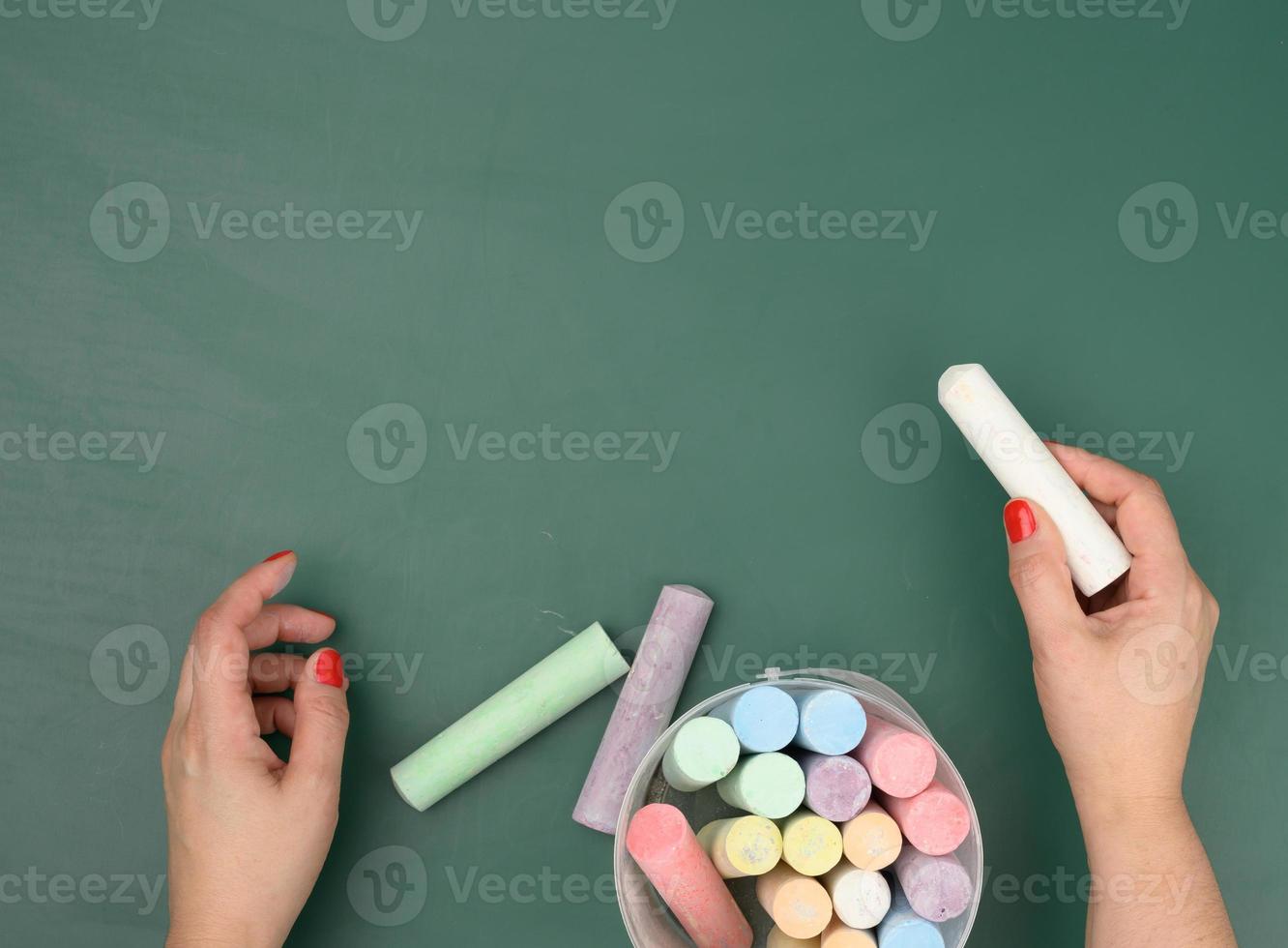 hand holds a piece of white chalk on the background of an empty green chalk board photo