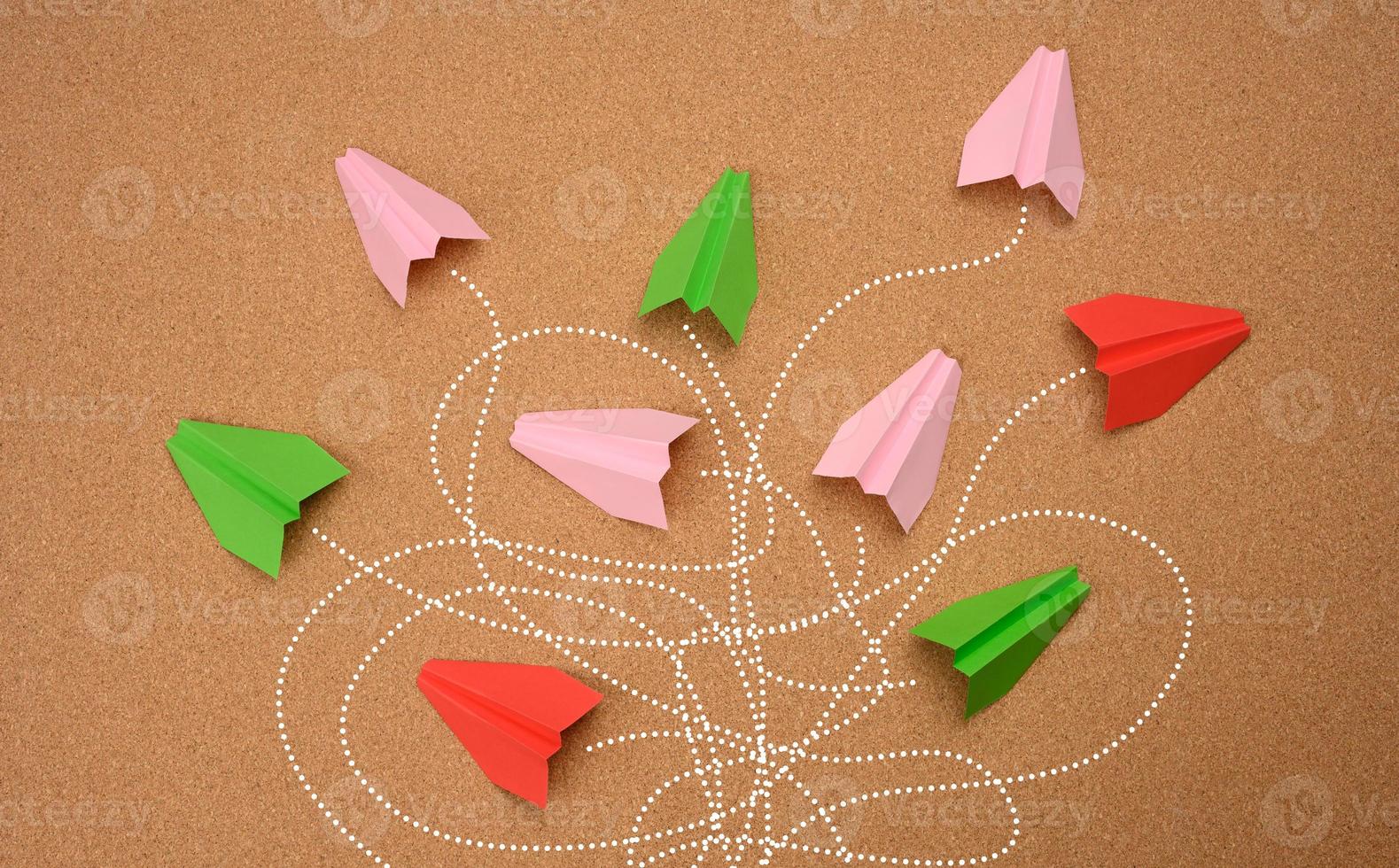 grupo de aviones de papel multicolores con largos caminos enredados sobre un fondo marrón. foto