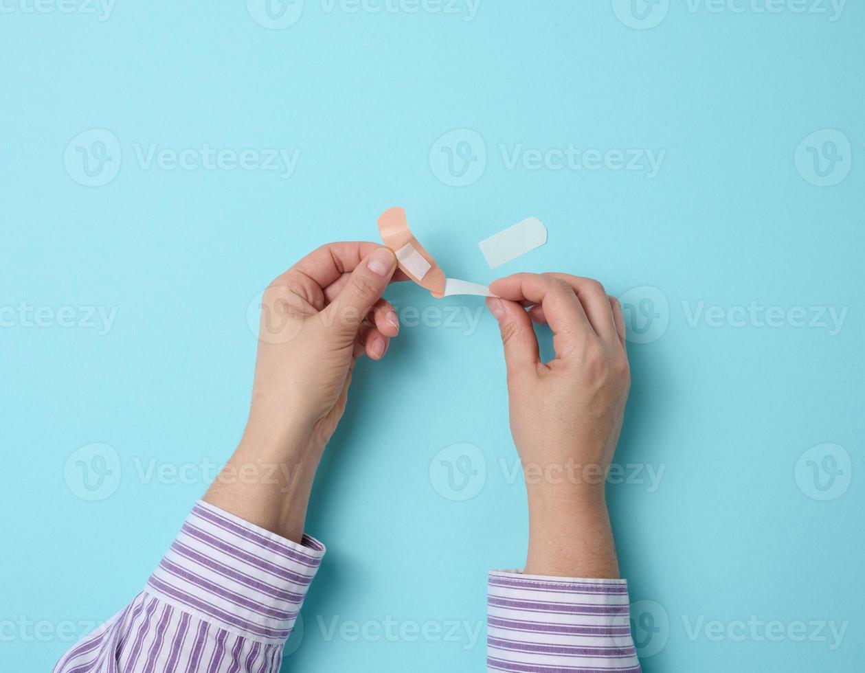 female hand and brown medical adhesive plaster for the treatment of injuries and cuts on the skin, blue background photo