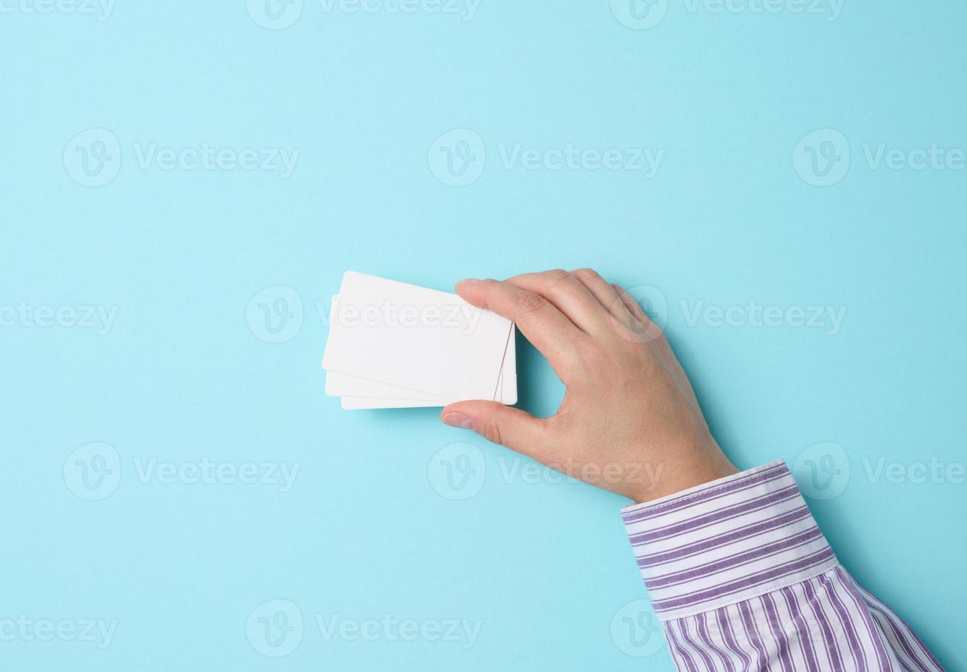 Female hand holding empty paper white business card on a blue background. Copy space photo