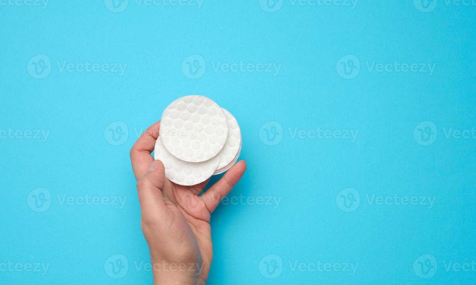 female hand holding clean round white cotton makeup remover pads on blue background photo