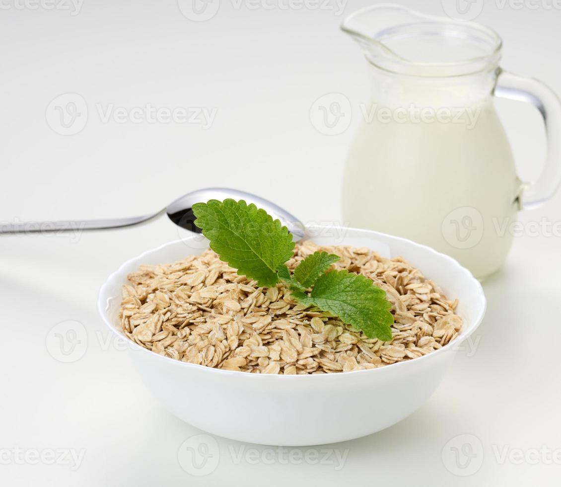 Milk and white bowl with dry oatmeal on a white background, breakfast photo