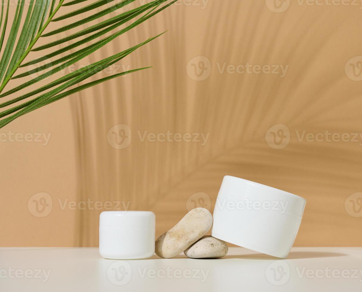 frasco de plástico redondo blanco para productos cosméticos sobre un fondo marrón. sombra de hoja de palma. en blanco para productos de marca, maqueta foto