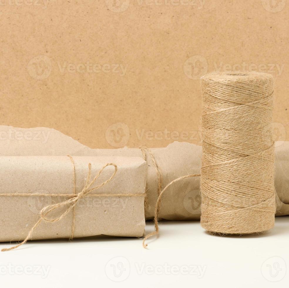 box, roll of brown kraft paper and reel with brown rope on white table, packing material photo