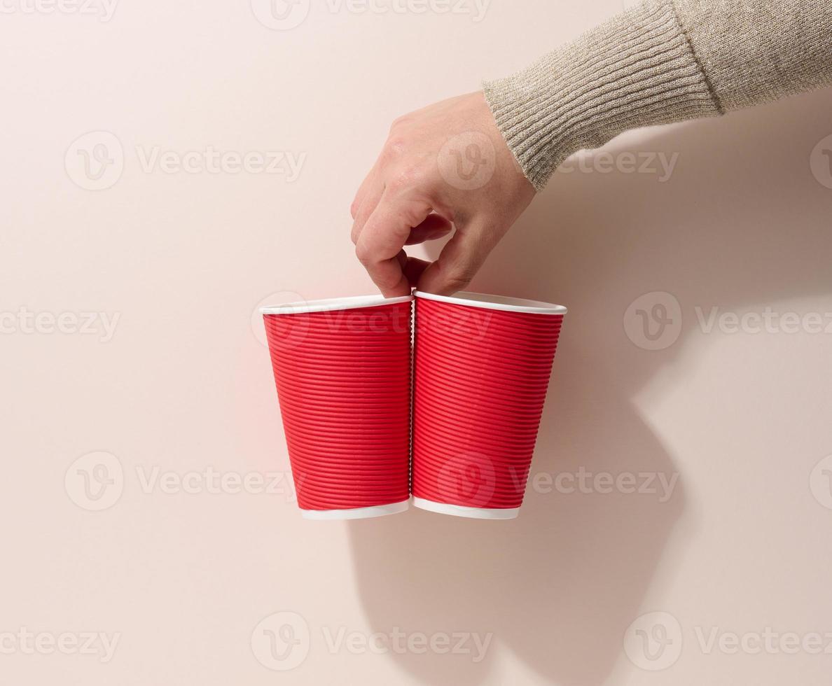 hand holds paper cardboard red cups for coffee, beige background. Eco-friendly tableware, zero waste photo