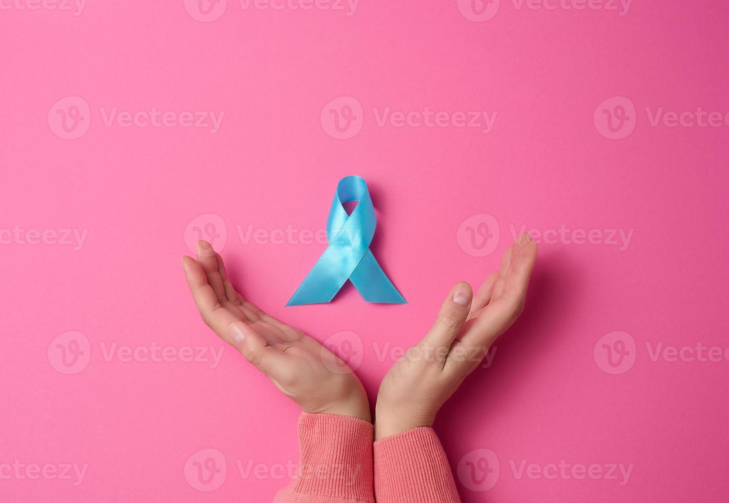 woman hands holding light blue ribbon awareness on a pink background. Men's health and prostate cancer awareness campaign concept. photo