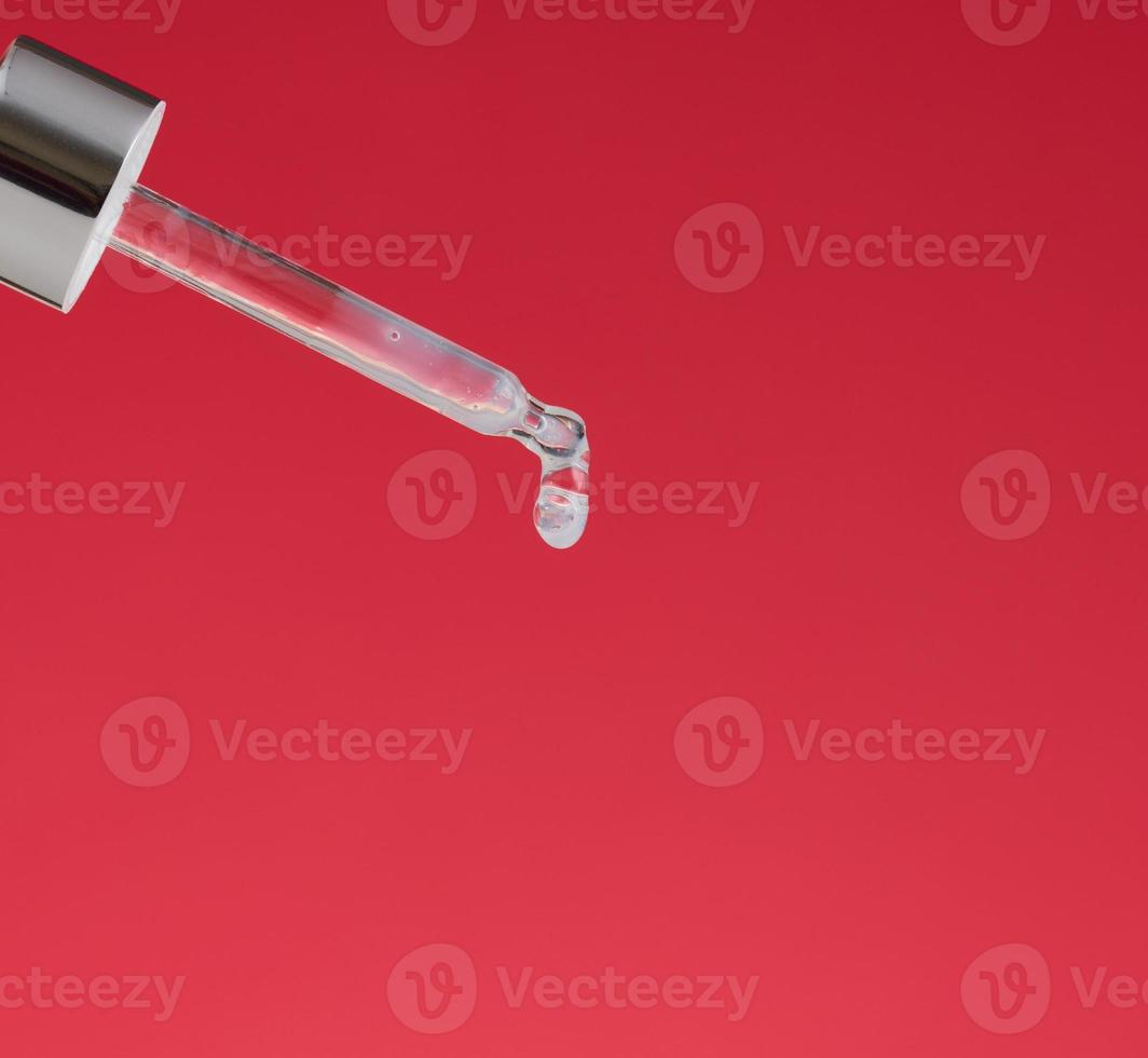 glass pipette with dripping transparent liquid on a red background. Acid, serum photo