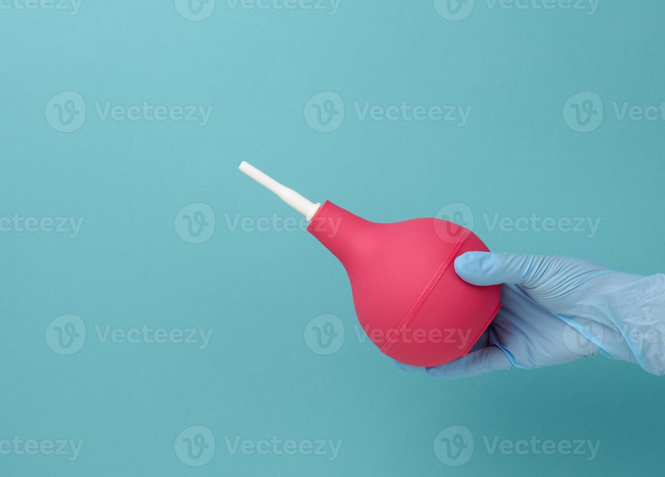 a hand in a blue medical glove holds a pink rubber enema on a blue background photo