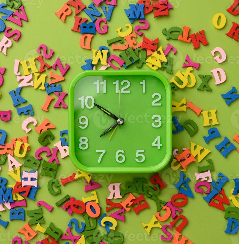 square alarm clock and multicolored wooden letters of the english alphabet on a green background photo
