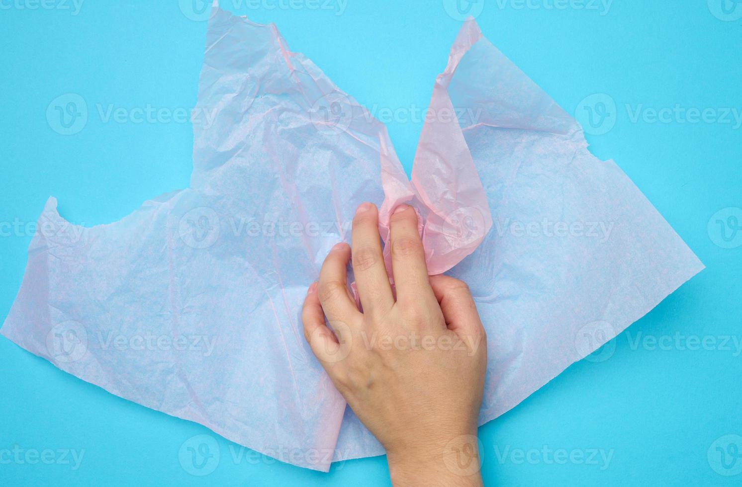 female hand hold pink folded wrapping crumpled paper on a blue background photo