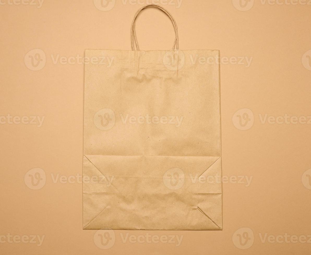 large disposable brown kraft paper bag with handles on a brown background, eco packaging, zero waste photo