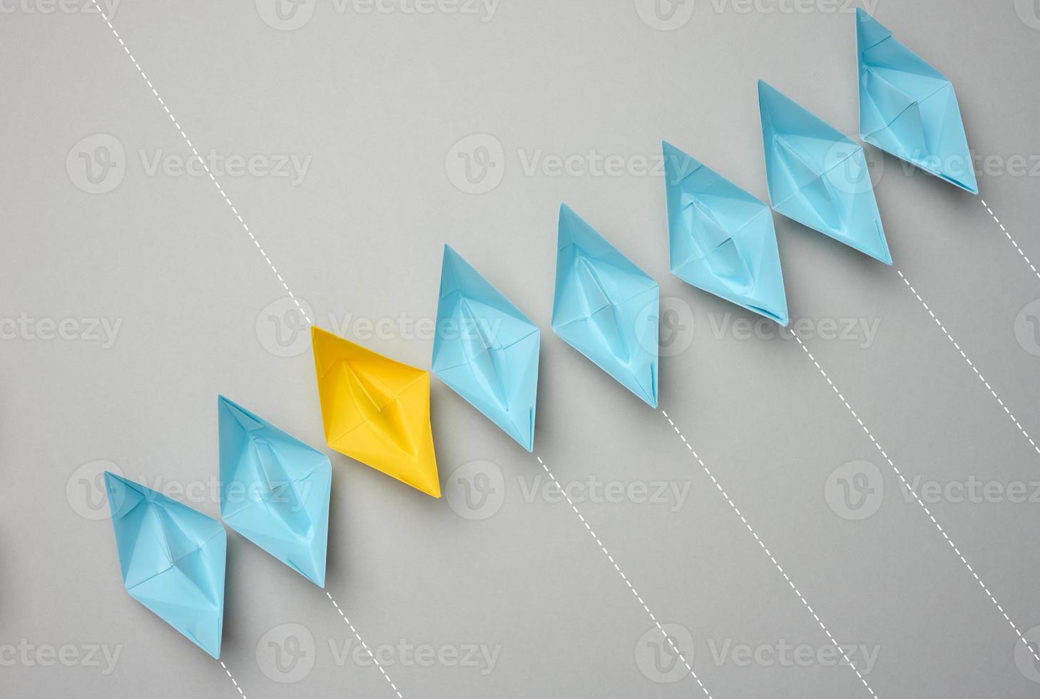 A row of paper boats on a gray background, yellow is moving in the opposite direction photo