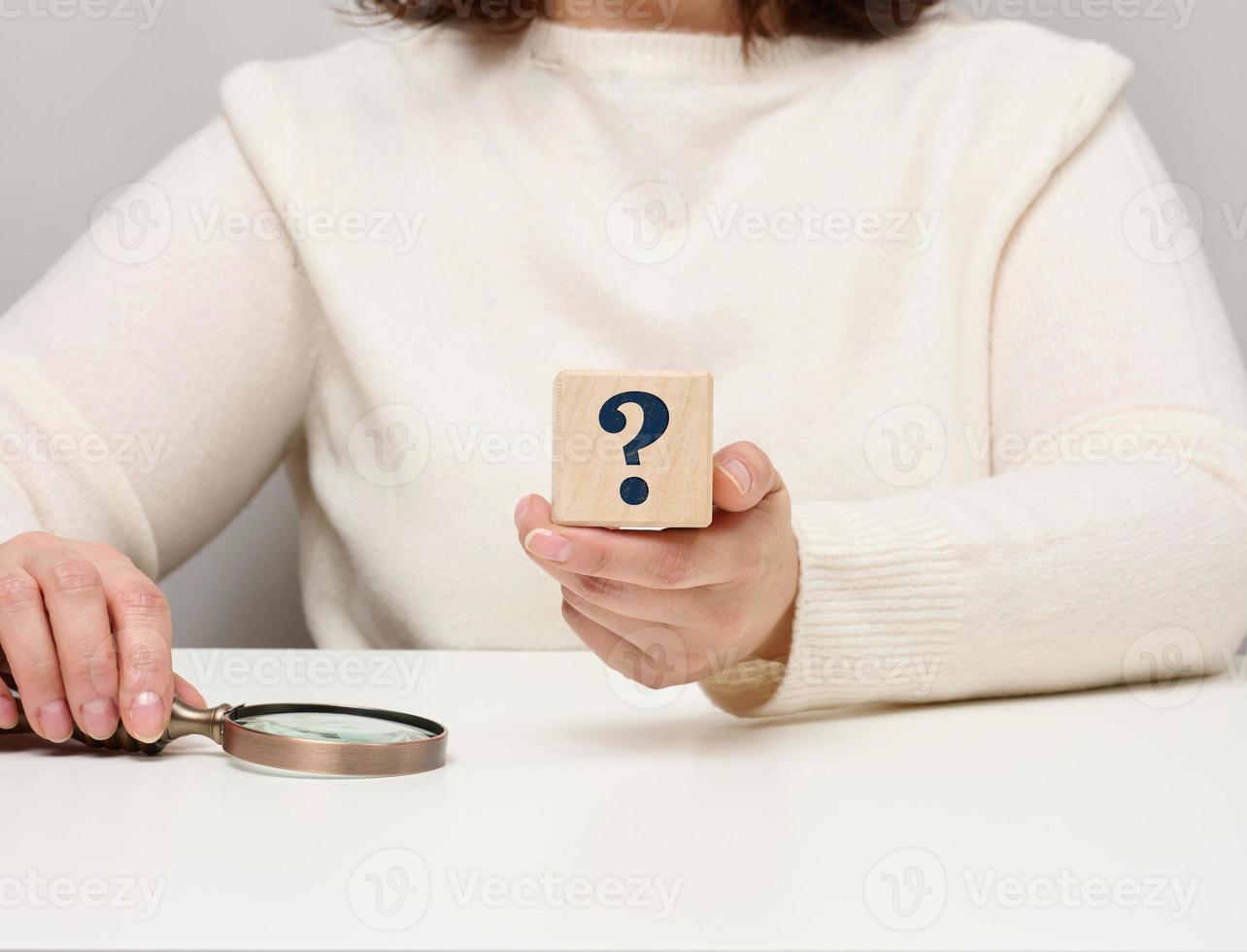 female hand holding a wooden cube with a question mark, concept of answers and questions, suspense and solution methods photo