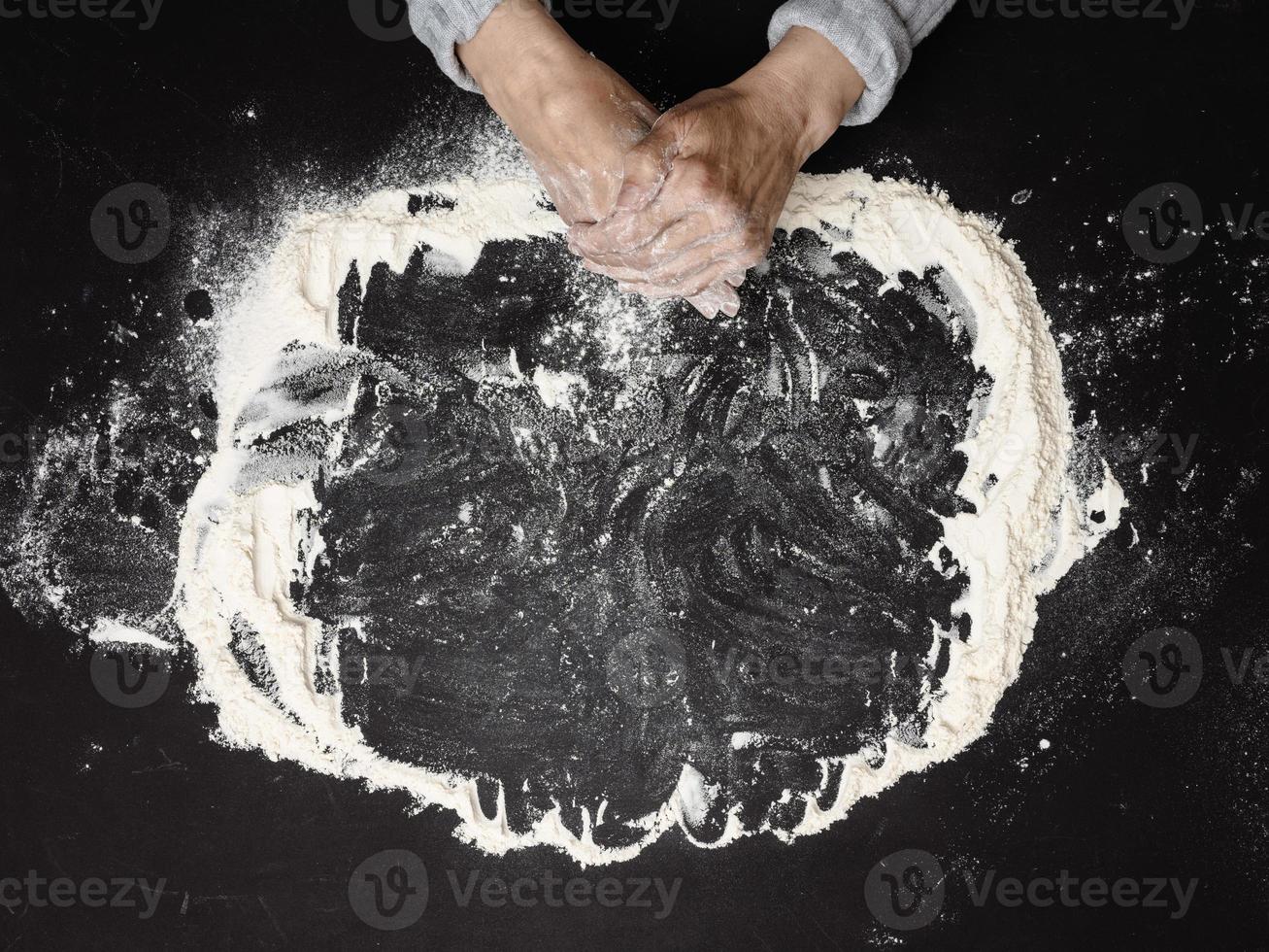 harina de trigo blanca tamizada sobre una mesa negra y dos manos femeninas, vista superior. cocinar en casa foto