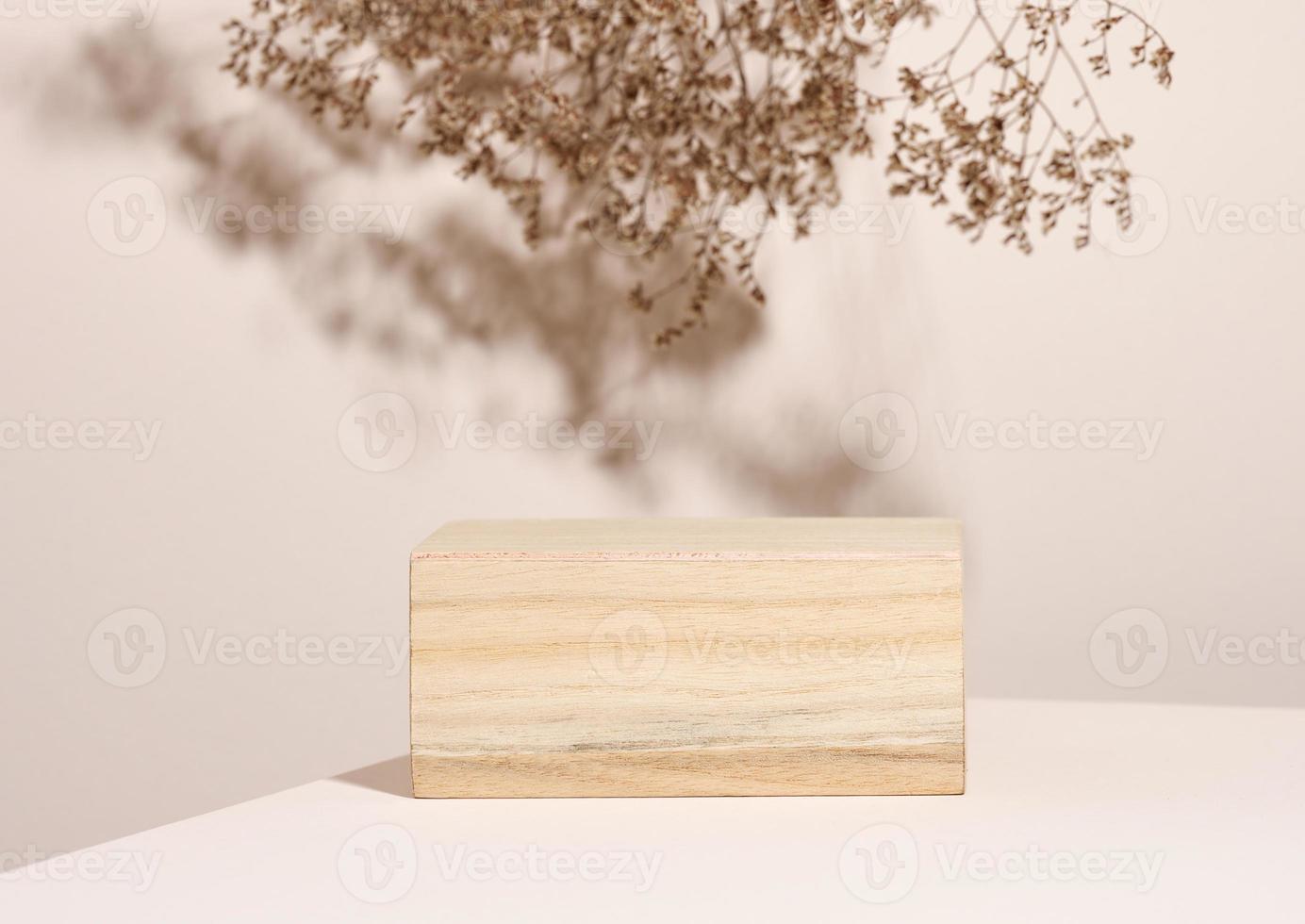 podio de madera para exhibir cosméticos y otros artículos, fondo beige con flores silvestres secas y sombra foto