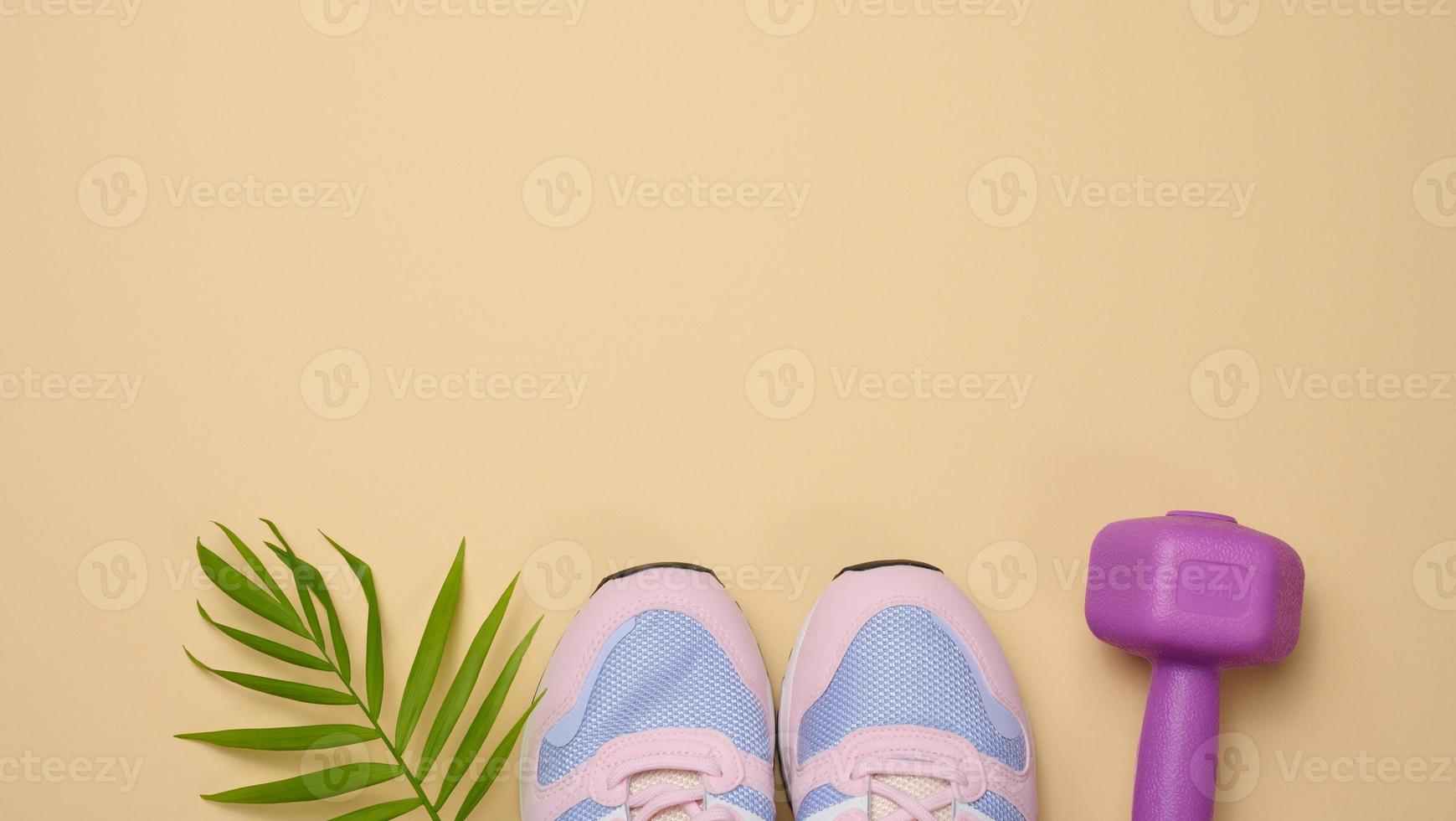 pair of pink sneakers and purple dumbbells on a beige background, sports. Copy space photo