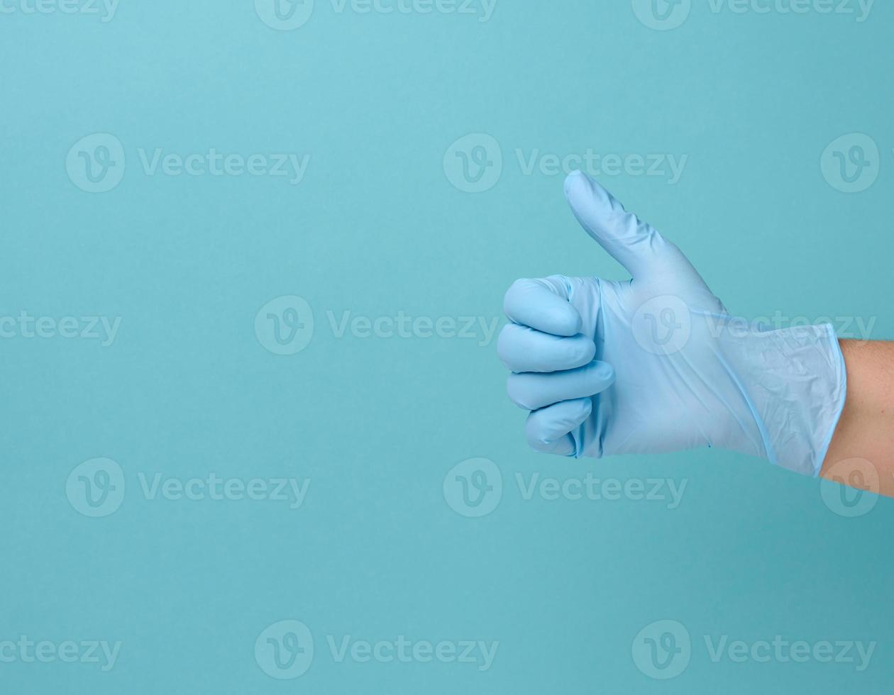 la mano en un guante médico desechable de látex azul muestra el gesto como en un fondo azul foto