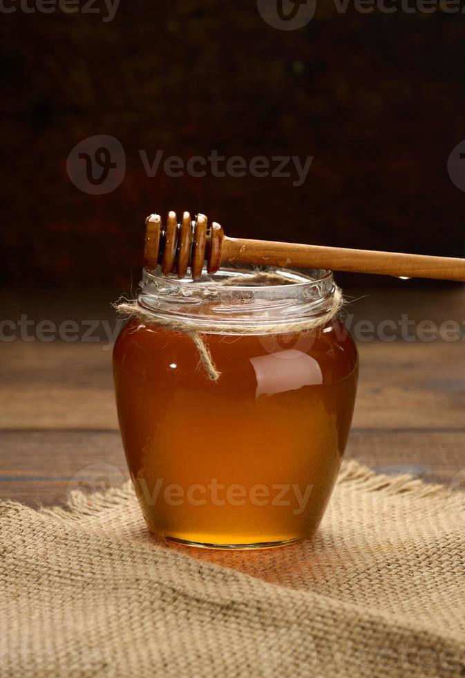 miel fresca en un frasco de vidrio transparente y una cuchara de madera sobre una mesa marrón foto