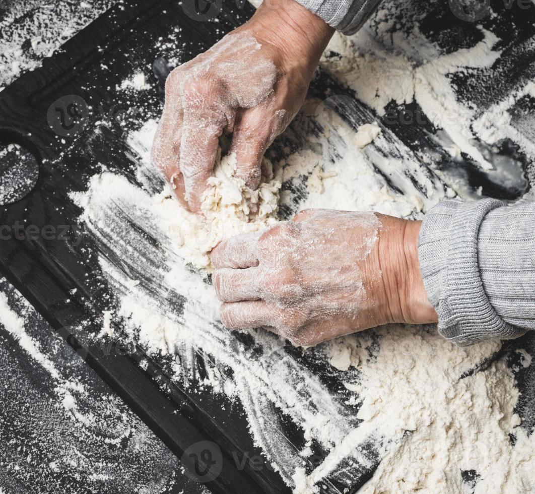 two female hands knead the dough from white wheat flour on a black table, top view photo