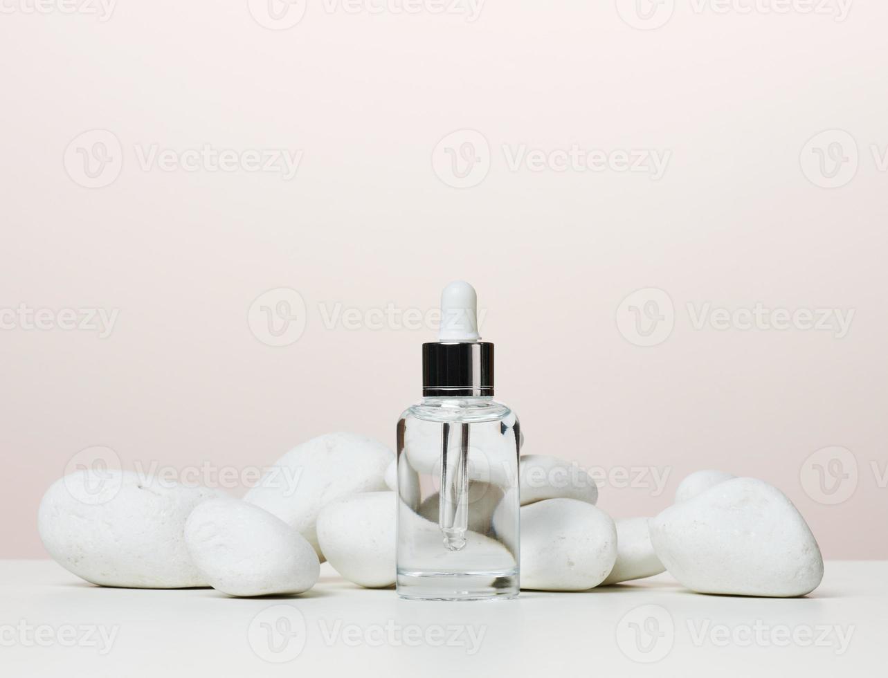 botella transparente de vidrio blanco con una pipeta para cosméticos, aceites, ácidos sobre una mesa blanca foto