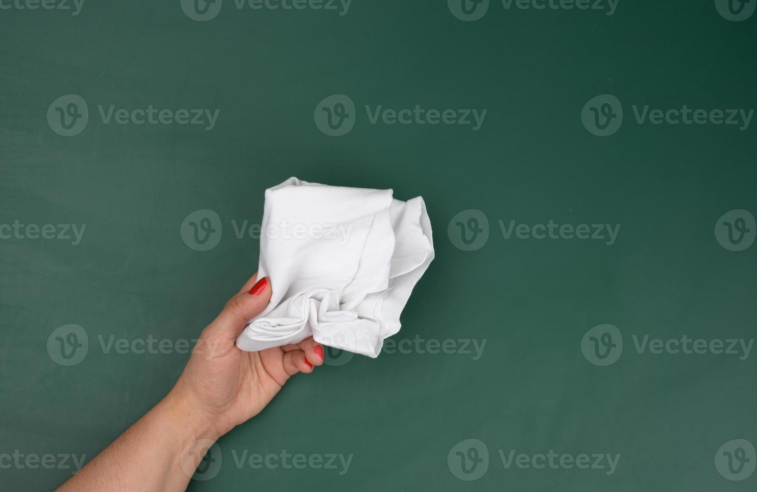 a woman's hand holds a white rag against the background of a green chalk board photo