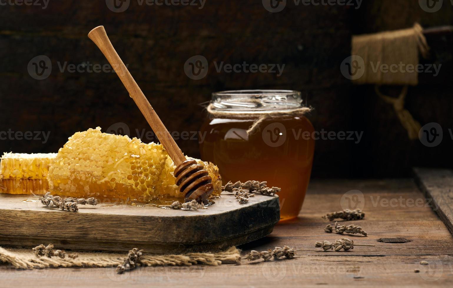 panal de cera con miel sobre una tabla de madera, detrás de un tarro de miel foto