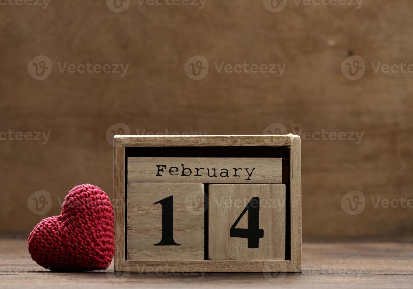 wooden calendar with date February 14 and red knitted heart, brown background photo