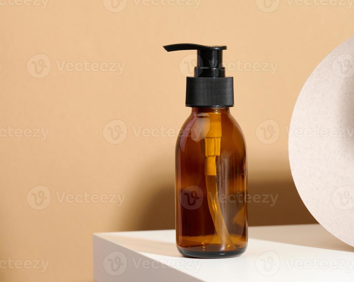 Brown glass bottle with black pump of cosmetic products on white table. Natural organic spa cosmetic, beauty concept. Mockup photo
