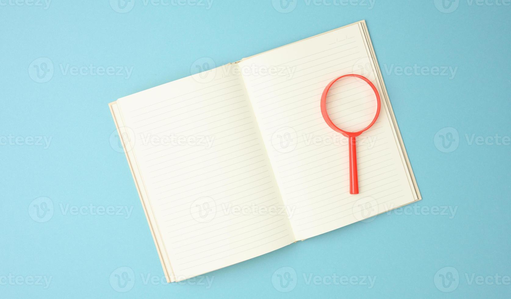 paper notebook with blank white sheets and a red magnifier on a blue background. Background for inscriptions photo