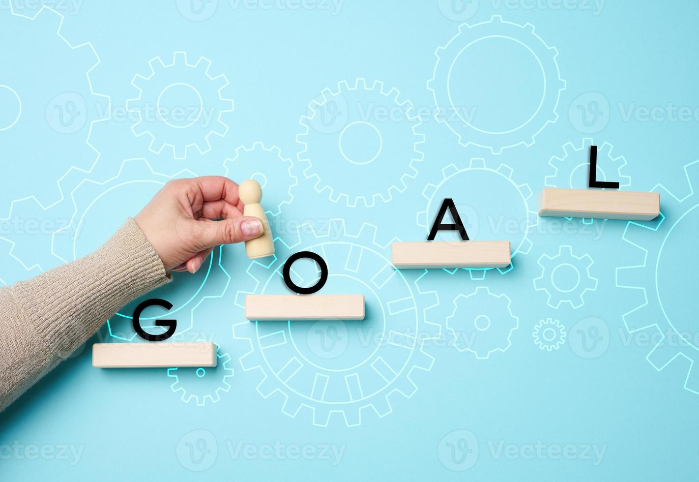 a female hand holds a wooden figurine on a blue background and wooden blocks. The concept of achieving the goal, the way forward photo