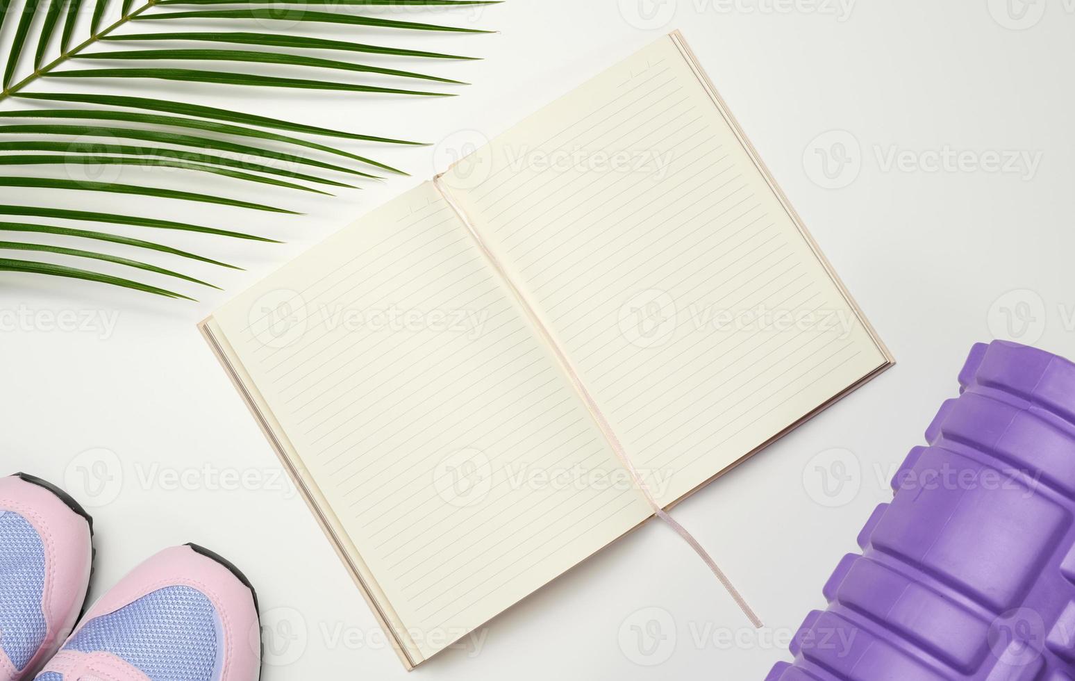 open blank notebook, a pair of sports gym shoes and dumbbells on a white background. Place for recording, top view photo