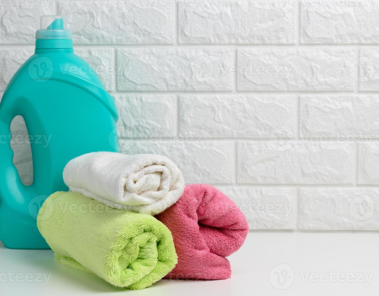 a plastic bottle of liquid washing powder and folded towels on a white shelf photo