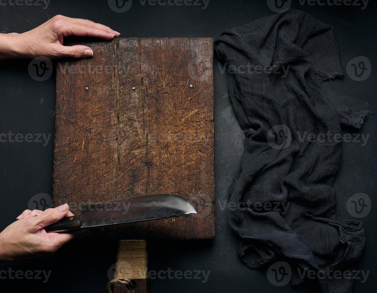 tabla de cortar de madera rectangular marrón vacía, mujer sosteniendo un cuchillo grande sobre una mesa negra, vista superior foto