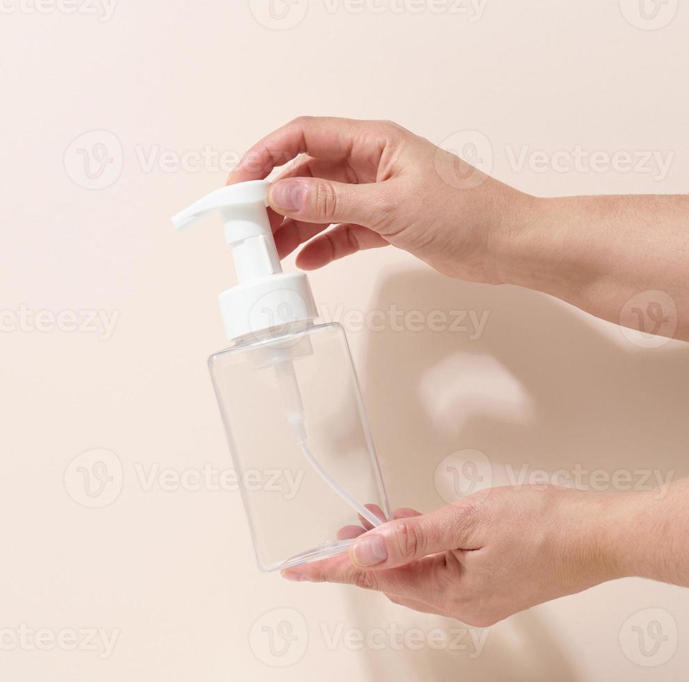 female hand holds empty plastic container with dispenser for liquid products, soap or shampoo on beige background photo