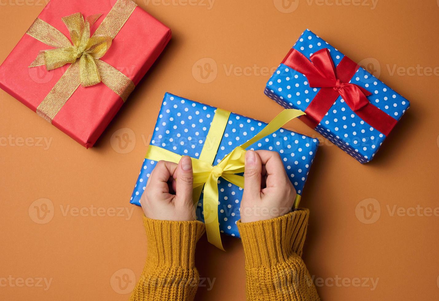 female hand holds a box wrapped with gift paper on an orange background. Christmas preparation photo