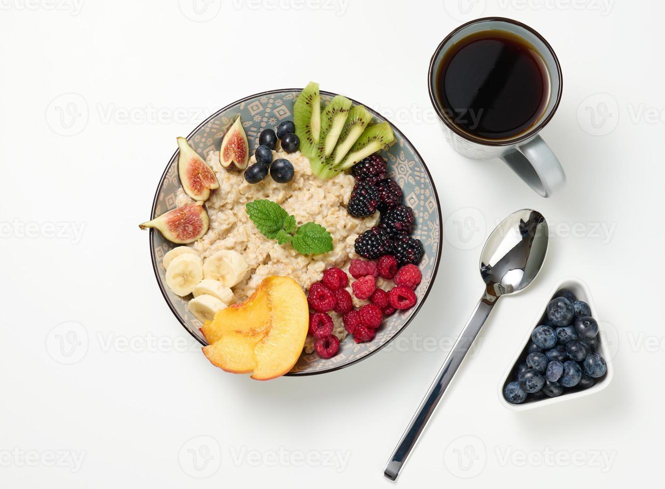 cup of coffee and boiled oatmeal with fruits in a round plate on a white table, top view. photo